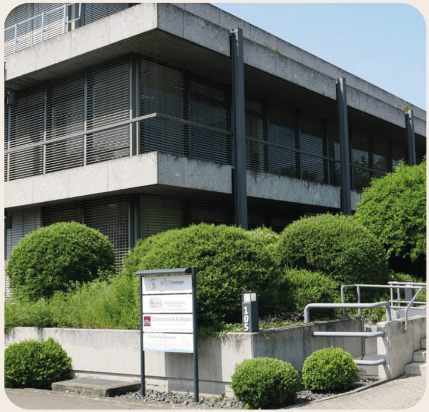Moderne Bürogebäude mit Glasfenstern, begrüntem Umfeld und einem Eingangsschild.